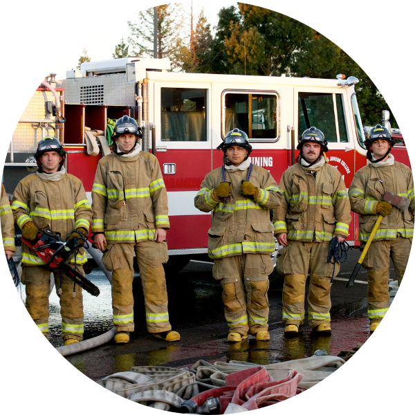 five fire technology students standing in full uniform in front of a red and white fire engine 